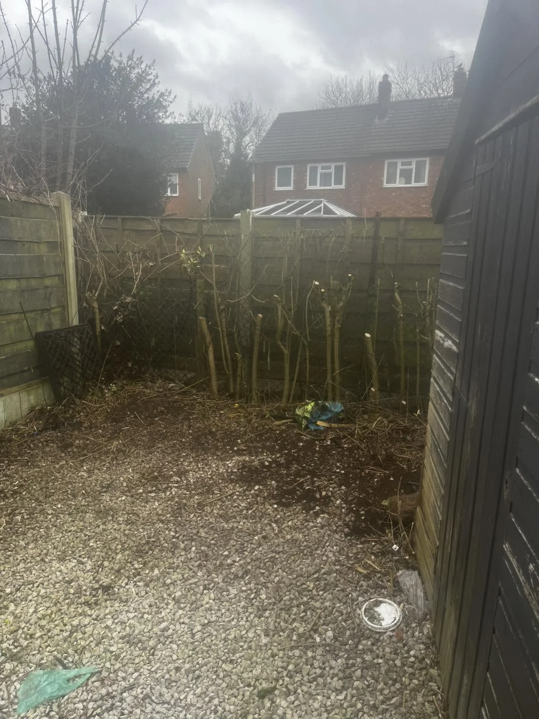 After clearance: vegetation cut back beside a dark timber shed, revealing the gravel area