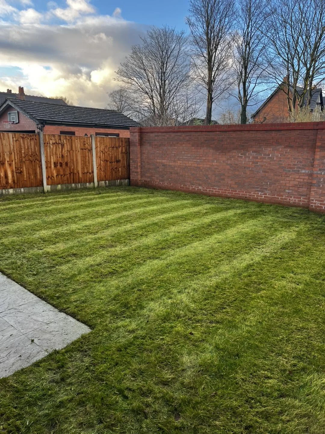 Freshly mown lawn beside timber fencing and a brick wall